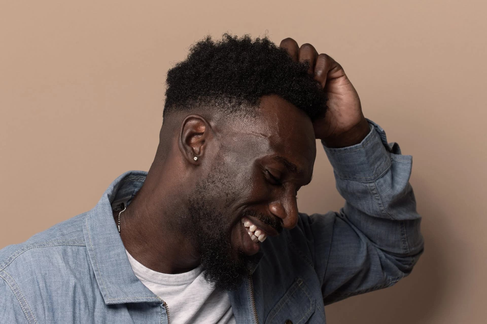 A man in the middle of laughing, one hand resting in his hair